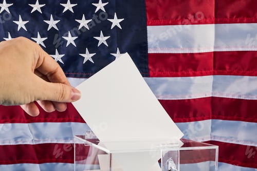 Preview: Hand putting his vote into ballot box against national flag of United States