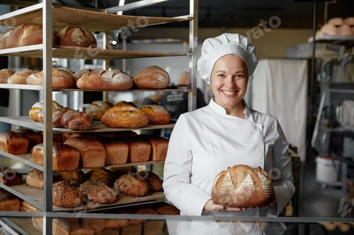 Preview: Happy woman baker chef holding bread standing near showcases