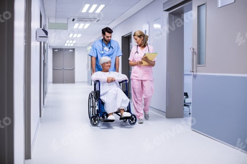 Preview: Male and female doctor interacting with female senior patient on wheelchair in corridor