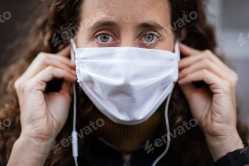 Preview: Caucasian woman putting on a protective mask in the streets and looking at the camera