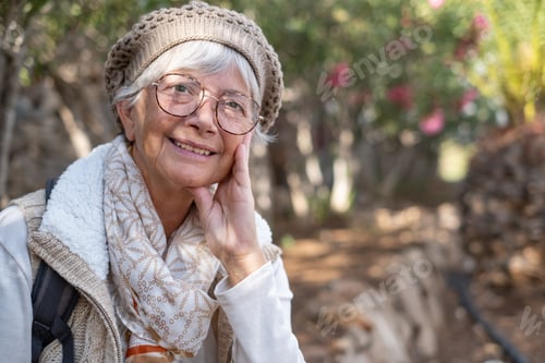 Preview: Portrait of senior attractive woman wearing glasses and cap sitting outdoors in public park