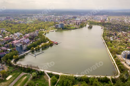 Preview: Aerial view of city lake among green trees and town buildings in recreation park zone. Drone