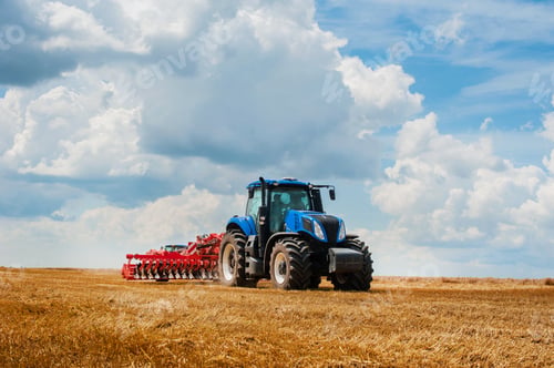 Preview: New blue tractor in motion at demonstration field site at agro exhibition working with harrows.