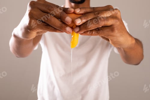 Preview: Midsection of man breaking egg shell against gray background