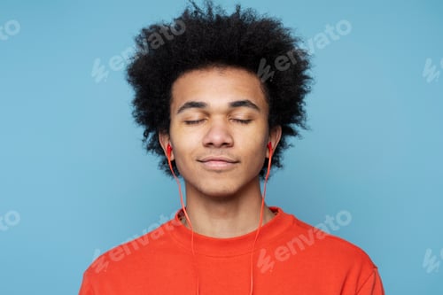 Preview: Smiling African American man wearing headphones listening music with eye closed. Technology concept