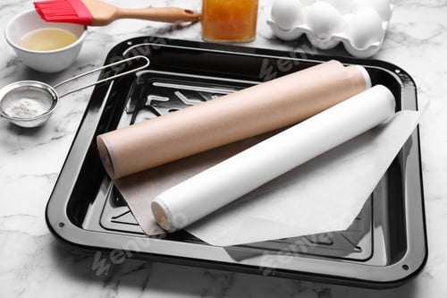 Preview: Baking pan with parchment paper, different ingredients and kitchen tools on white marble table