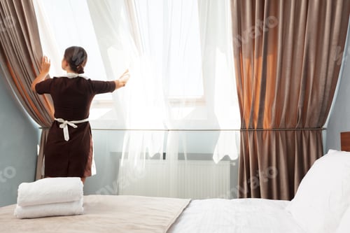 Preview: Woman opening curtains in a hotel room during the morning light