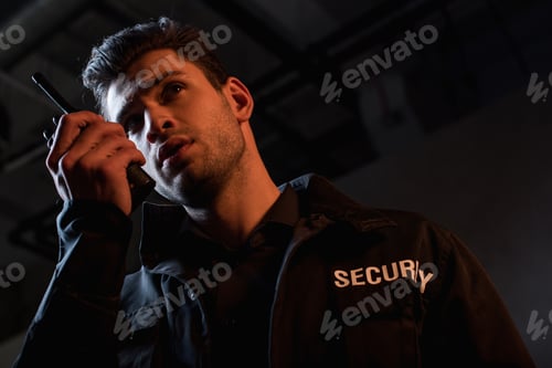 Preview: handsome guard in uniform using walkie-talkie and looking away