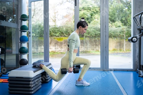 Preview: Fitness woman performing bulgarian split squat exercise with dumbbells in gym