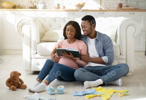 Preview: Cheerful expectant couple writing list of baby stuff for maternity hospital in living room