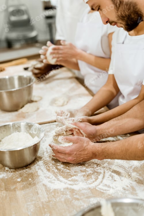 Preview: cropped shot of group of baking manufacture workers kneading dough together