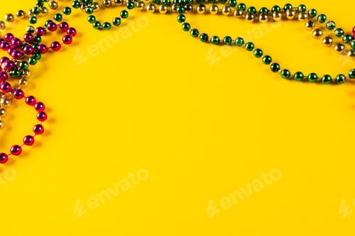 Preview: Composition of colourful mardi gras beads on yellow background with copy space
