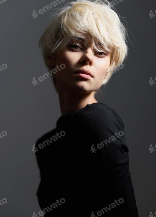 Preview: Thoughtful young woman with short blonde hair, posing against a dark background, exuding a sense of