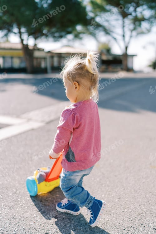 Preview: Little girl pushes a toy cart down the road in the park. Back view