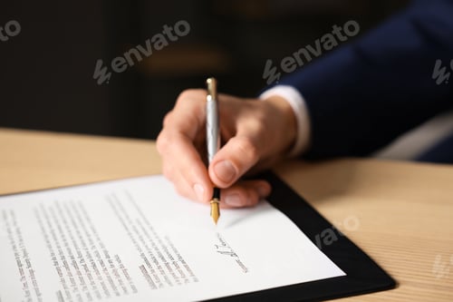 Preview: Man putting signature on document at wooden table, closeup