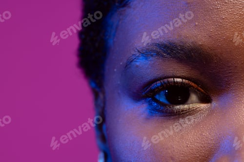 Preview: Close up of eye of african american woman with short hair in blue light on purple background