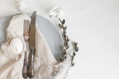 Preview: Stylish Easter table setting flat lay. Easter egg, willow branches, feathers on modern plate