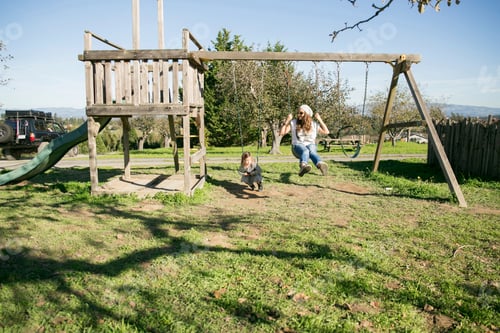Preview: A joyful moment as a parent pushes a child on a swing in a sunny park.
