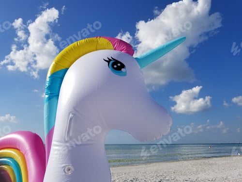 Preview: A close-up of the head of a blow-up rainbow unicorn float sitting on a Florida beach with a bright