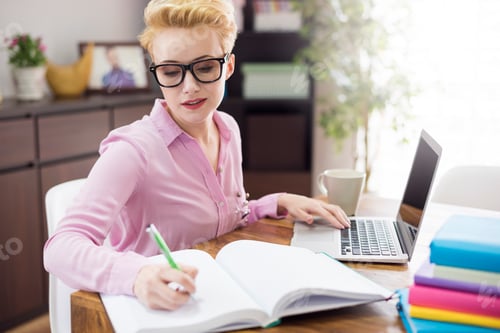 Preview: Woman using laptop and writing notes on desk