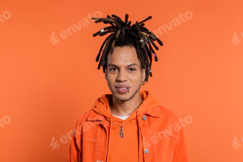 Preview: portrait of pierced multiracial man with dreadlocks looking at camera isolated on coral background