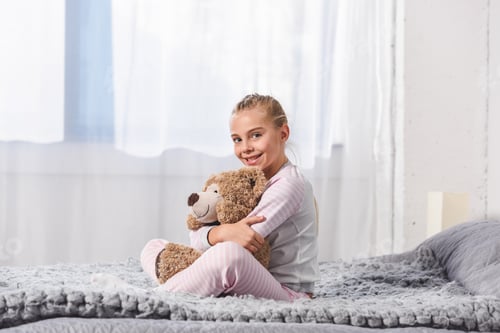 Preview: Cheerful kid holding teddy bear and sitting on bed