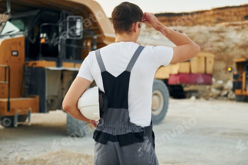 Preview: Rear view. Worker in professional uniform is on the borrow pit at daytime