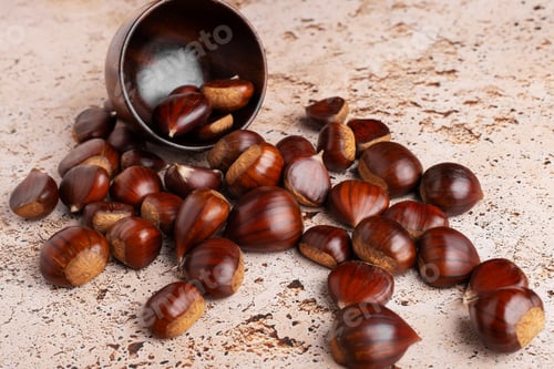 Preview: Autumn chestnuts in rustic wooden bowl on beige stone kitchen table