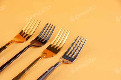 Preview: Half shot of elegant shiny stainless forks on isolated golden background with free space