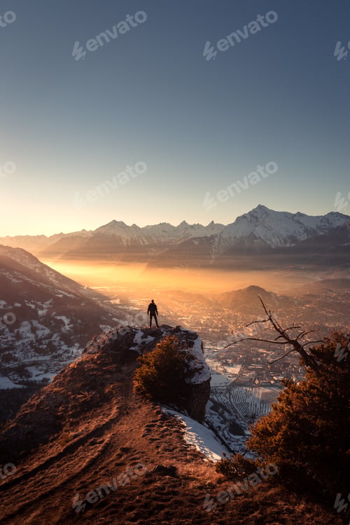 Preview: Winter landscape view of a silhouette standing on a rock over a foggy valley at sunset