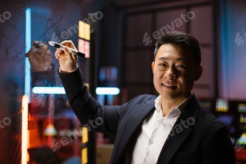 Preview: Asian businessman ceo manager in formal wear, standing at glass board and writing project tasks