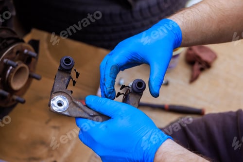 Preview: Man performs maintenance on a vehicle part while wearing blue gloves in a garage