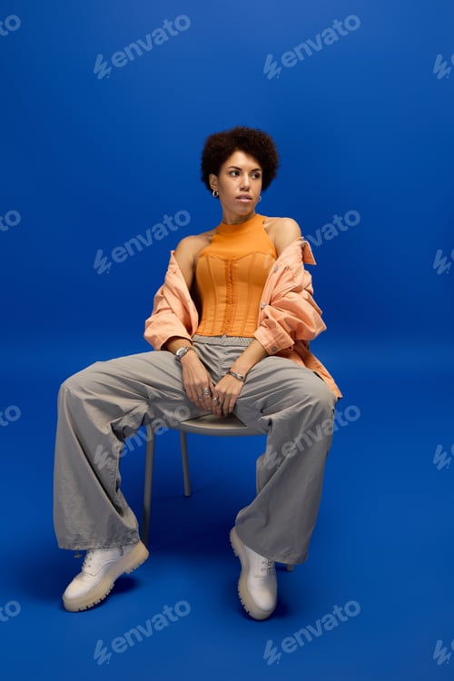 Preview: Elegant young woman in stylish attire posing confidently against a vibrant blue background