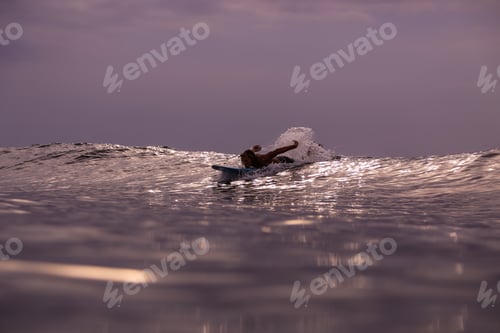 Preview: Man on surf board on waving water at sunset
