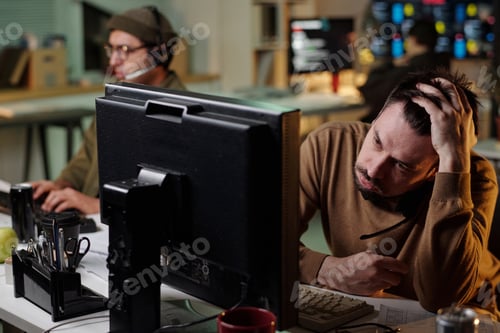 Preview: Young Caucasian Man Working at Computer in Scam Call Center Looking Stressed