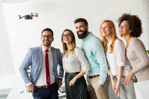 Preview: Young happy business people letting the drone camera to fly over the office and having fun