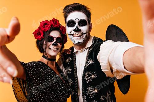 Preview: Cheerful man in sombrero making selfie with girlfriend in halloween. Funny guys with zombie makeup