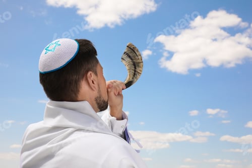 Preview: Jewish man in kippah and tallit blowing shofar outdoors. Rosh Hashanah celebration