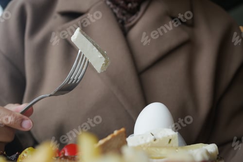 Preview: A person holds a fork with a piece of cheese. An egg is on the plate