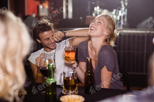 Preview: Cheerful friends holding beer mugs at nightclub
