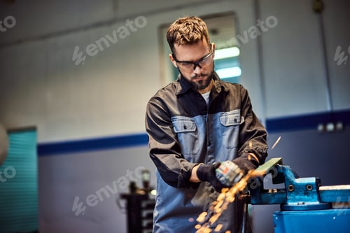 Preview: Focused mechanic wearing protective glasses, using a grinder to fix some metal parts.