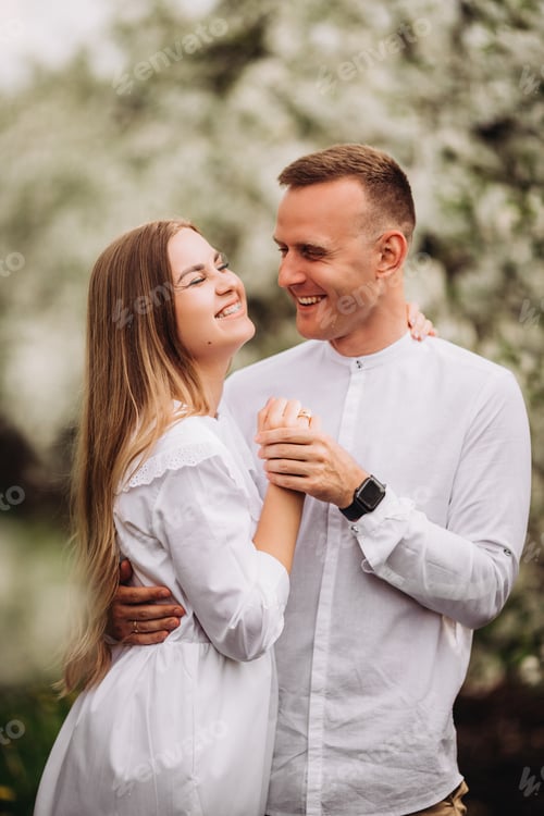 Preview: Young loving couple in a walk in a spring blooming apple orchard. Happy married couple enjoy
