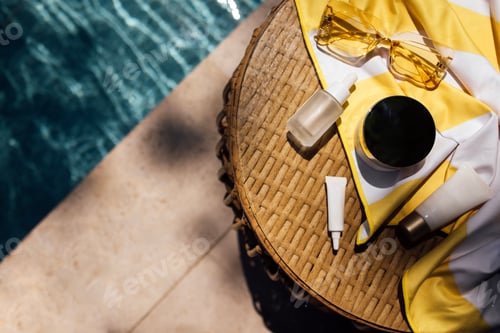 Preview: Skincare products arranged on a round wicker table beside a swimming pool