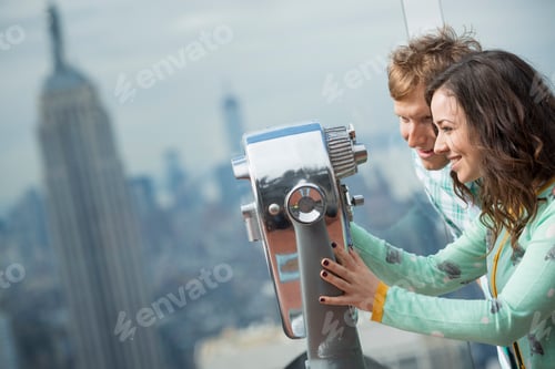 Preview: A couple looking through telescope on an observation deck overlooking the Empire State Building.
