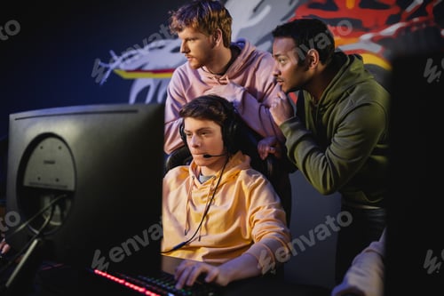 Preview: Interracial team standing near gamer playing video game on computer in cyber club