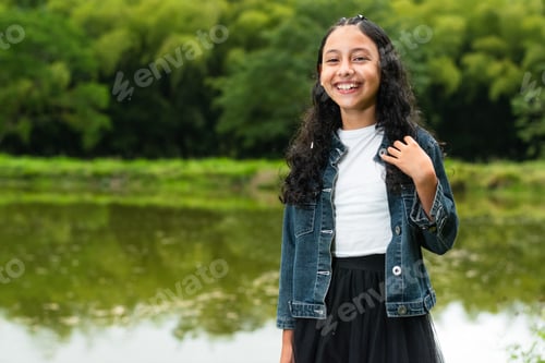 Preview: little brunette latina girl smiling happily with a fishing lake in the background