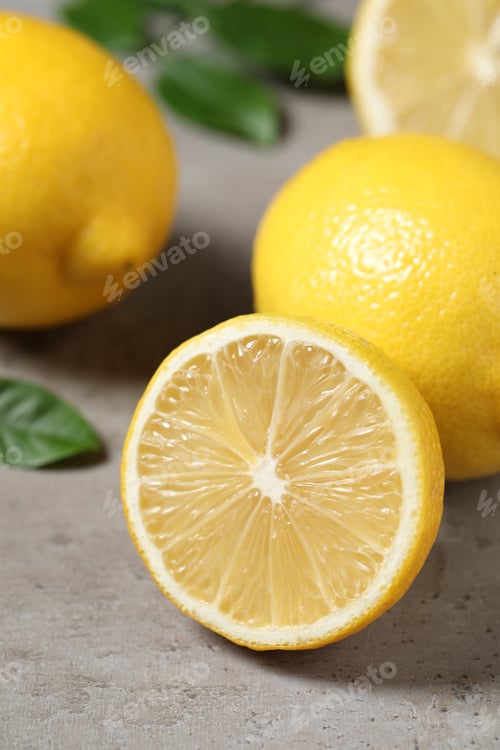Preview: Fresh lemons and green leaves on grey table outdoors, closeup
