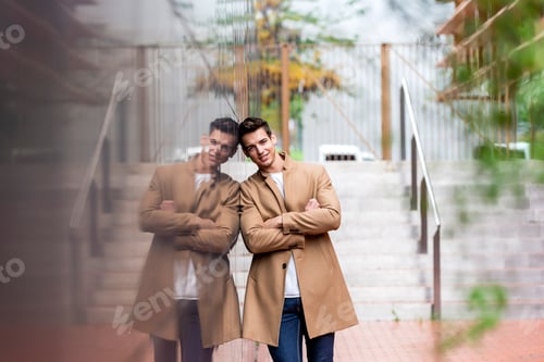 Preview: Portrait of stylish handsome young man with coat standing outdoors and leaning on wall.