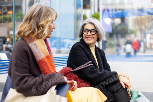 Preview: Senior women friends talking cheerfully at bus stop