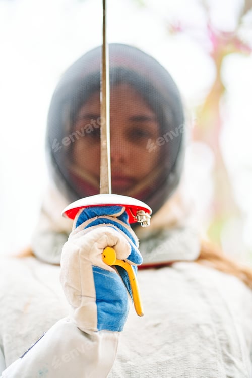 Preview: Portrait of woman dressed in white fencing costume practicing with the sword on white background.